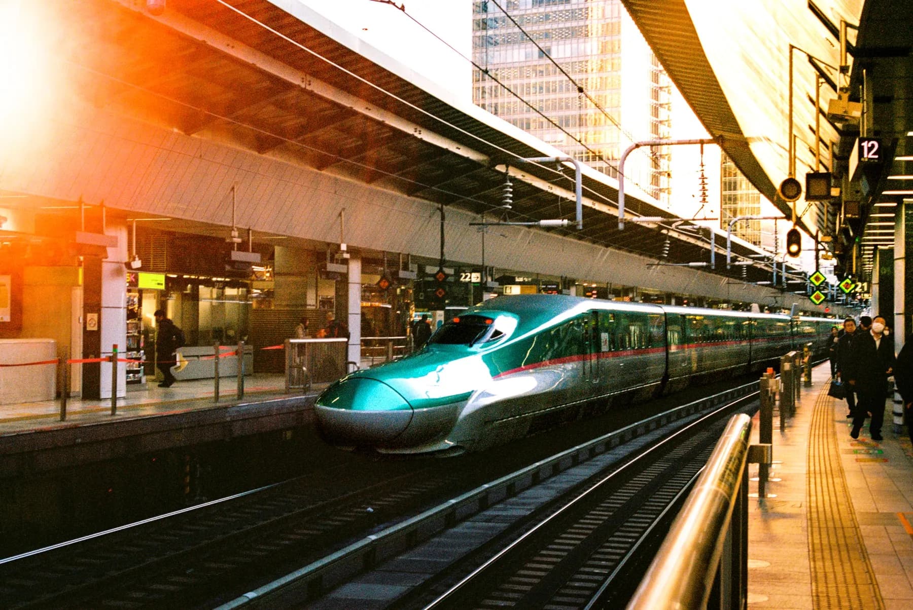 Green shinkansen arriving at a station platform in golden-hour light