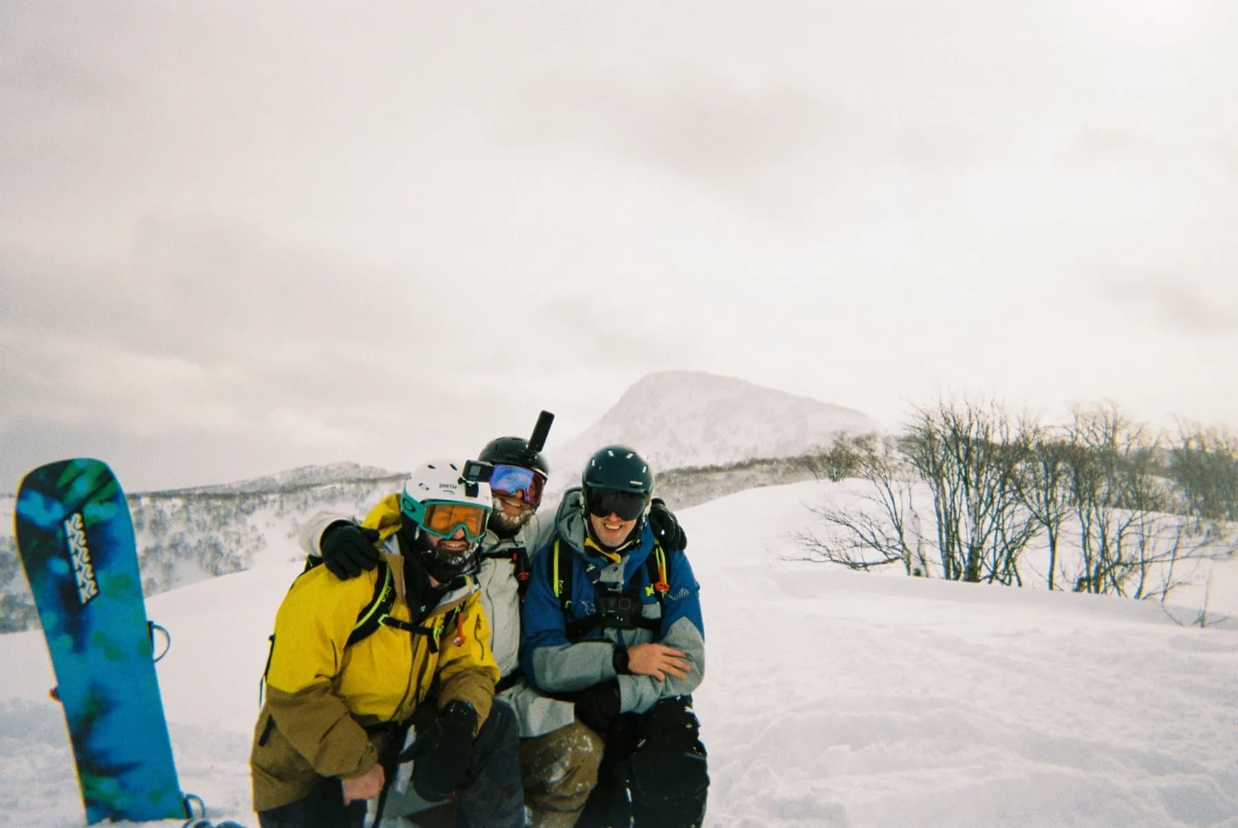 Two snowboarders resting in deep snow below Mount Yotei, shot on 35mm film