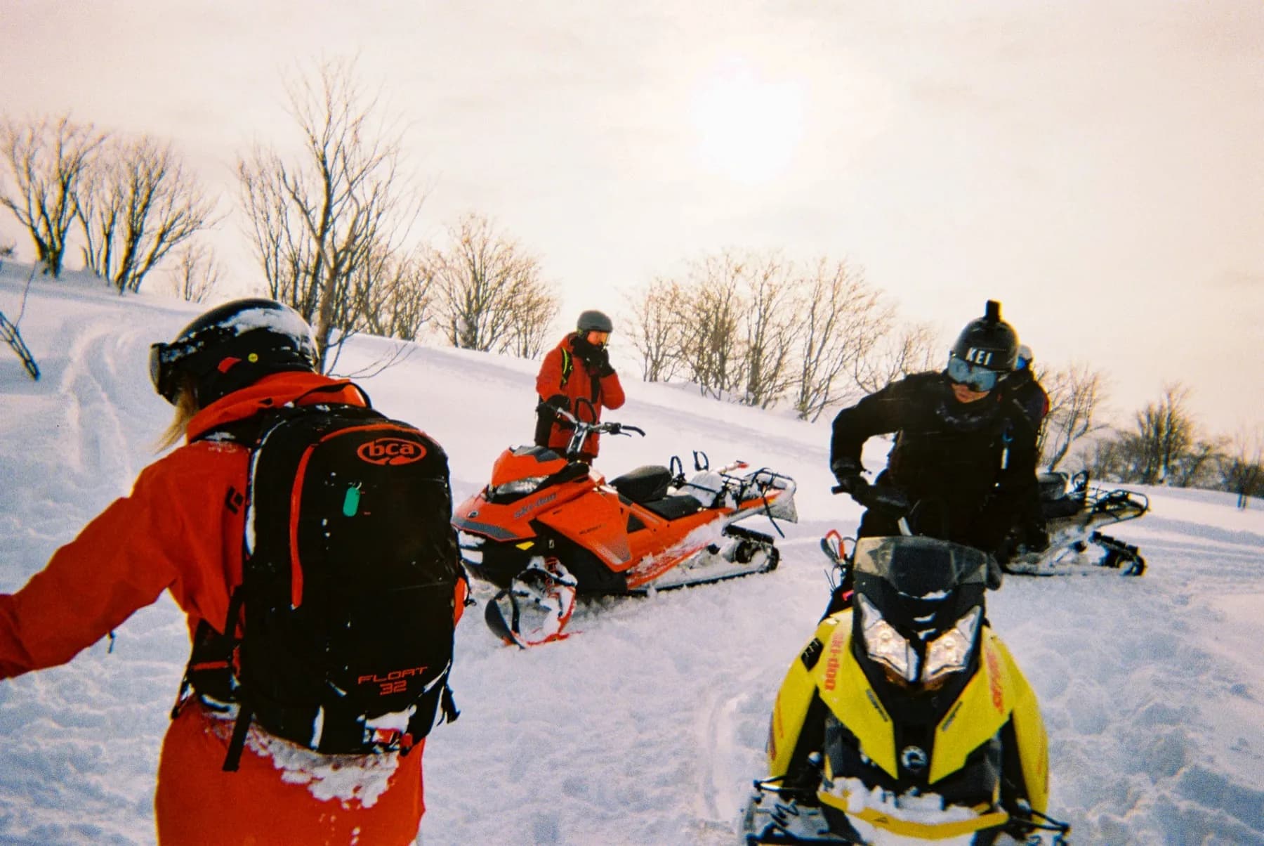 Backcountry crew loading snowmobiles in hazy winter sun