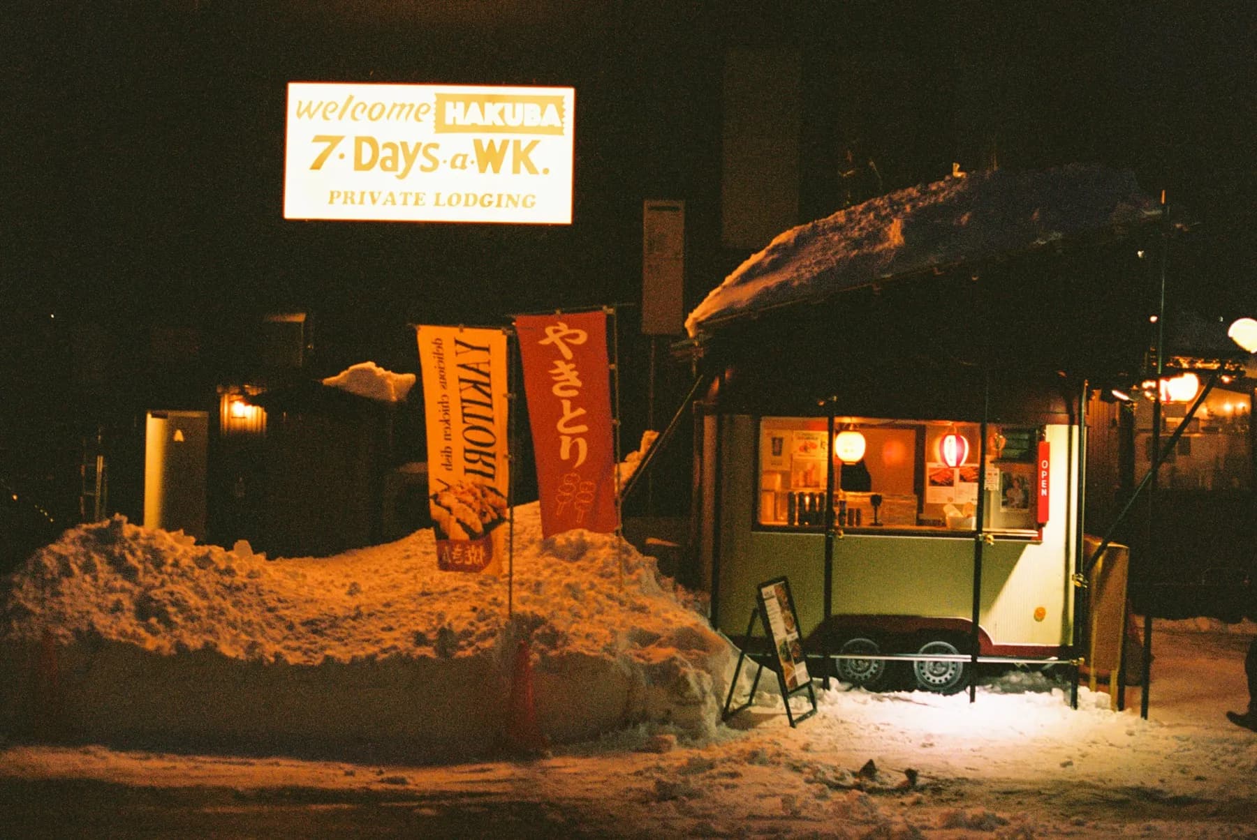 Yakitori stand glowing at night between snowbanks in Hakuba, Japan