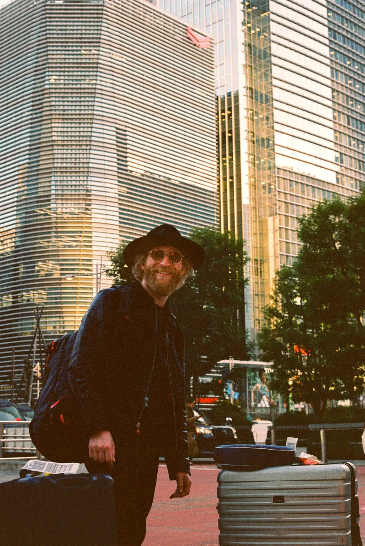 Film portrait of a traveler with a suitcase among Tokyo high-rises at golden hour
