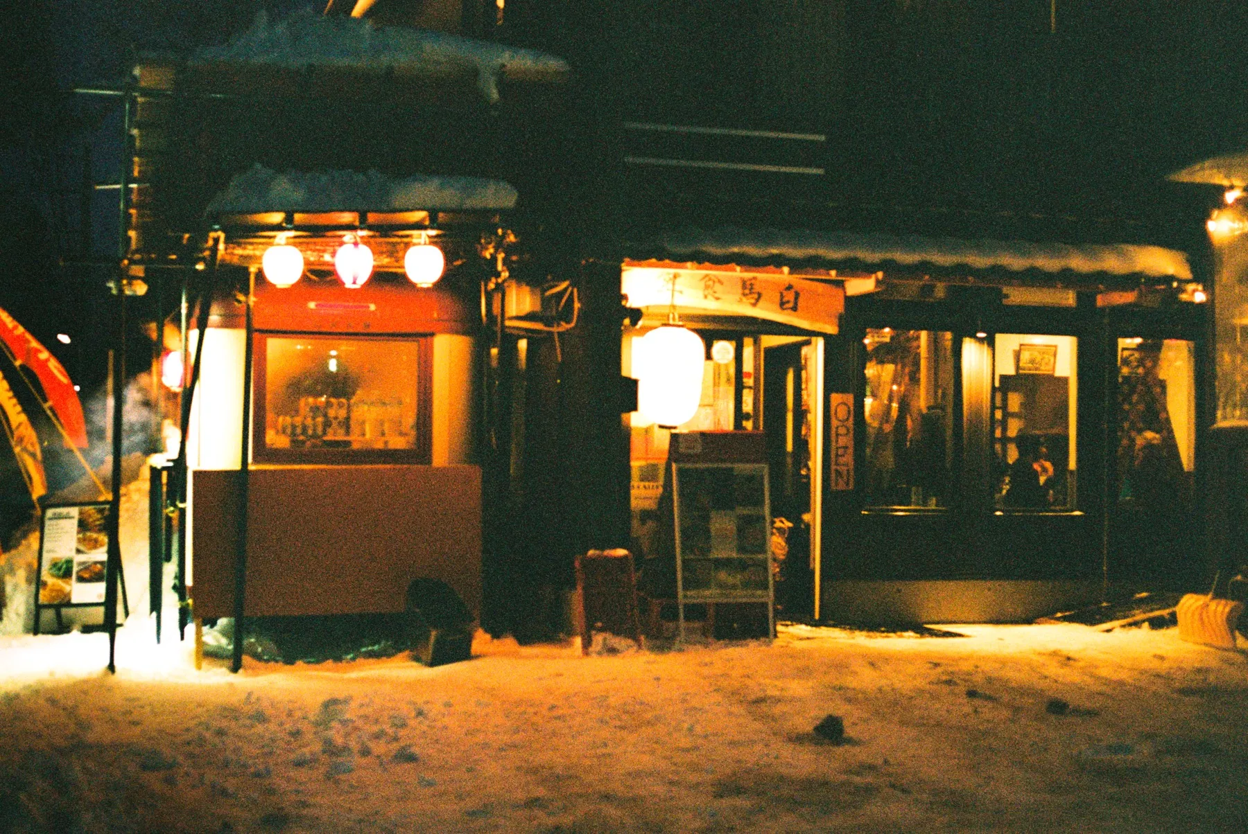 Lantern-lit food cart parked outside a restaurant on a snowy night