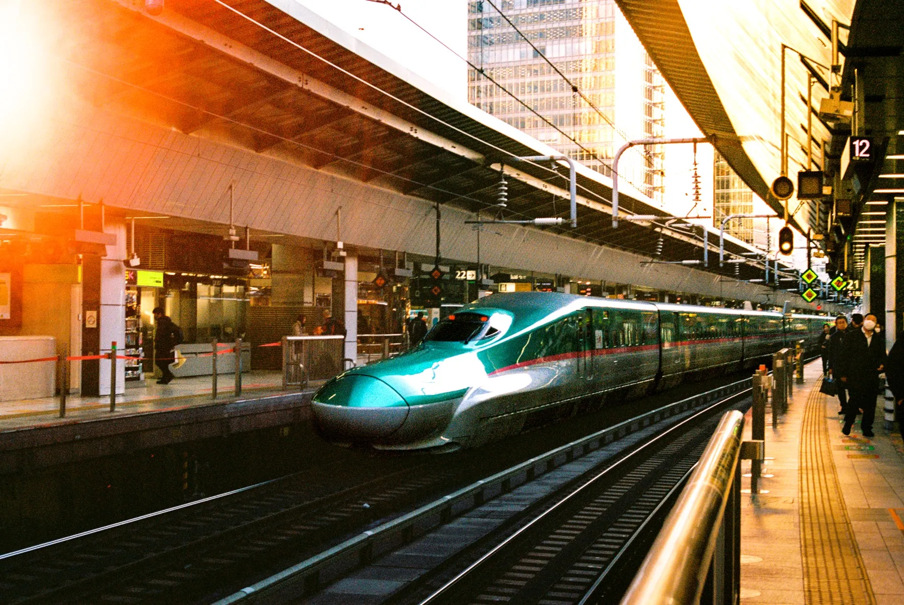 Green shinkansen arriving at a station platform in golden-hour light