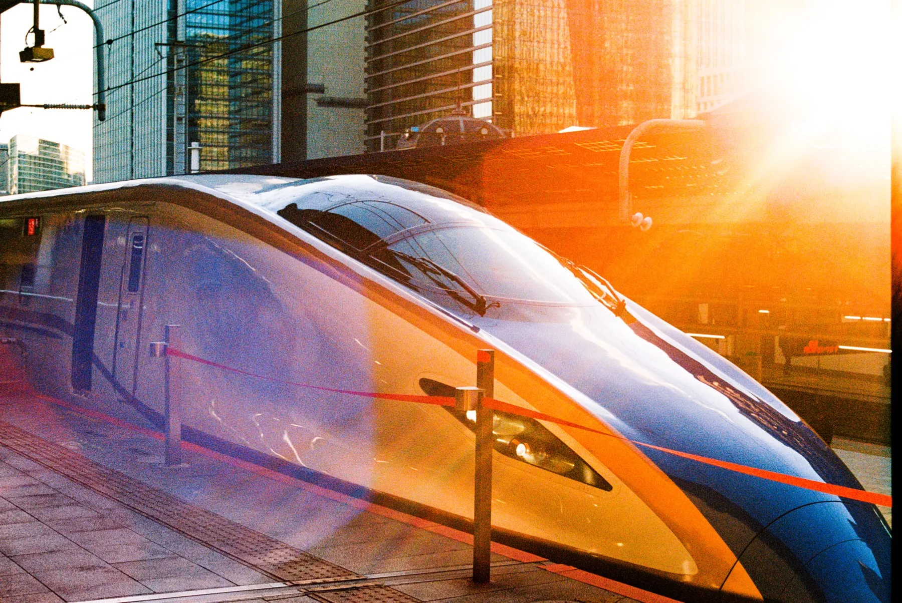 Shinkansen bullet train nose catching a sunburst on the platform