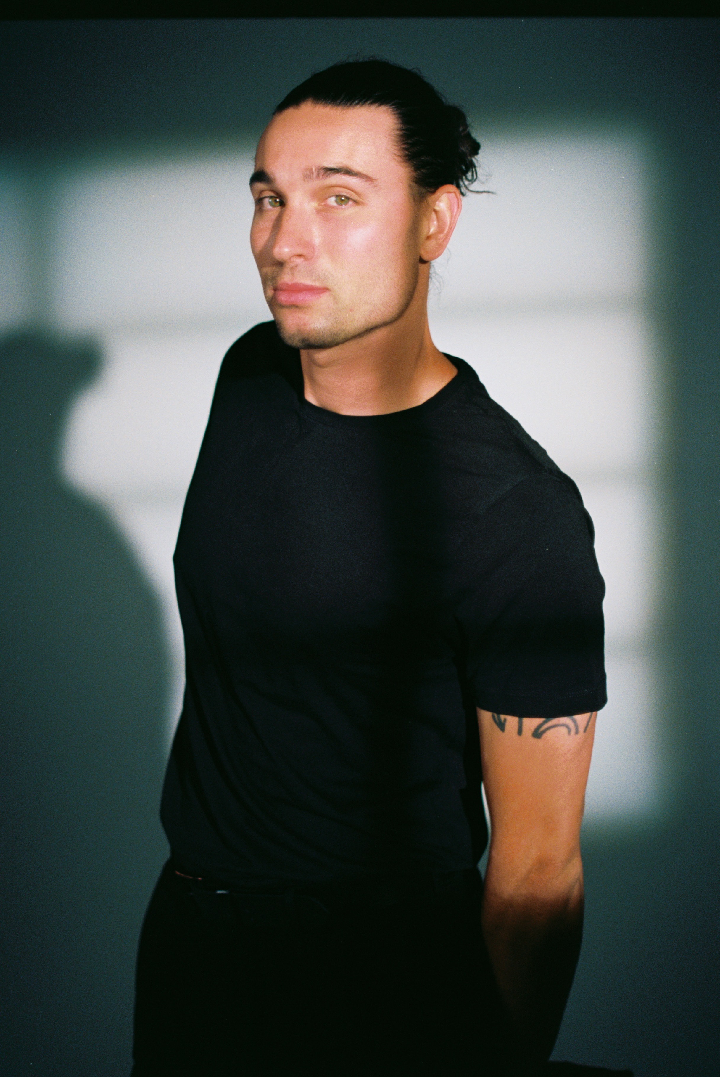 Editorial studio portrait on 35mm film, with a model in a black T-shirt casting a defined shadow against a gray wall.35mm film cinestill