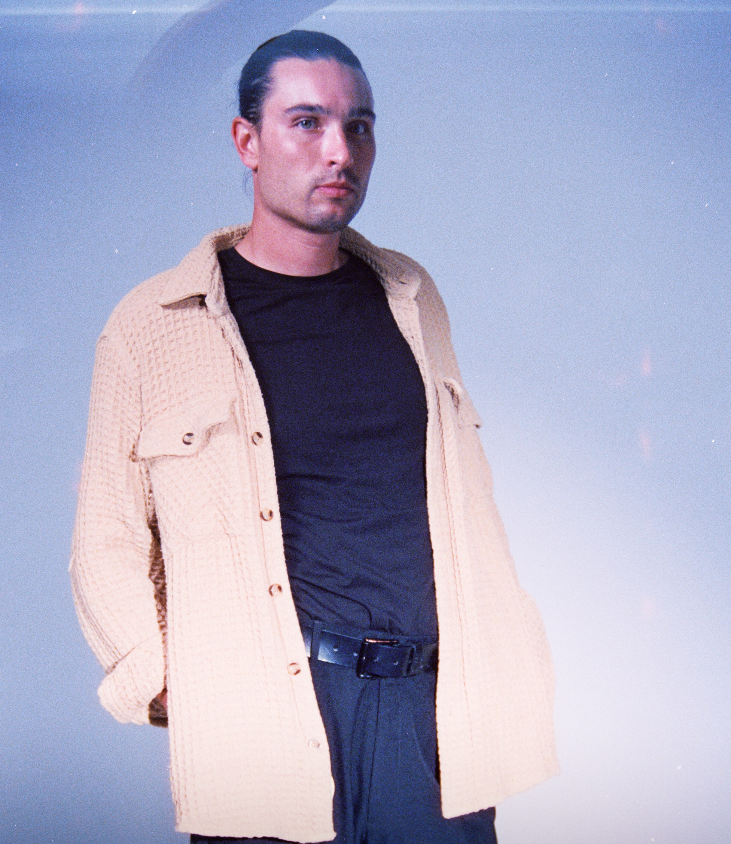 Studio film portrait of a model wearing a cream overshirt over a black T-shirt, looking off-camera against a cool blue backdrop. cinestill film, cine 8